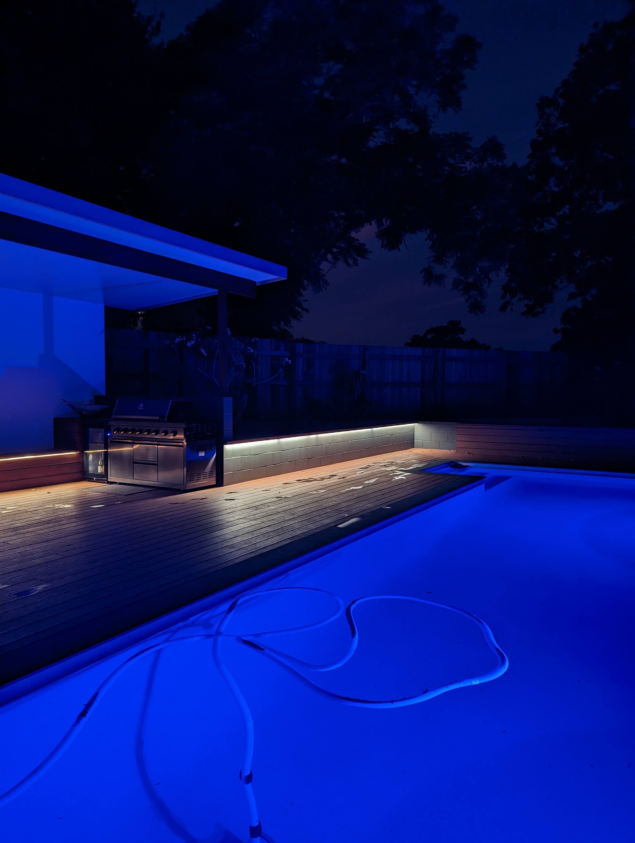 Deck and pool area lit at night with LED strip lighting along the deck edge and outdoor kitchen